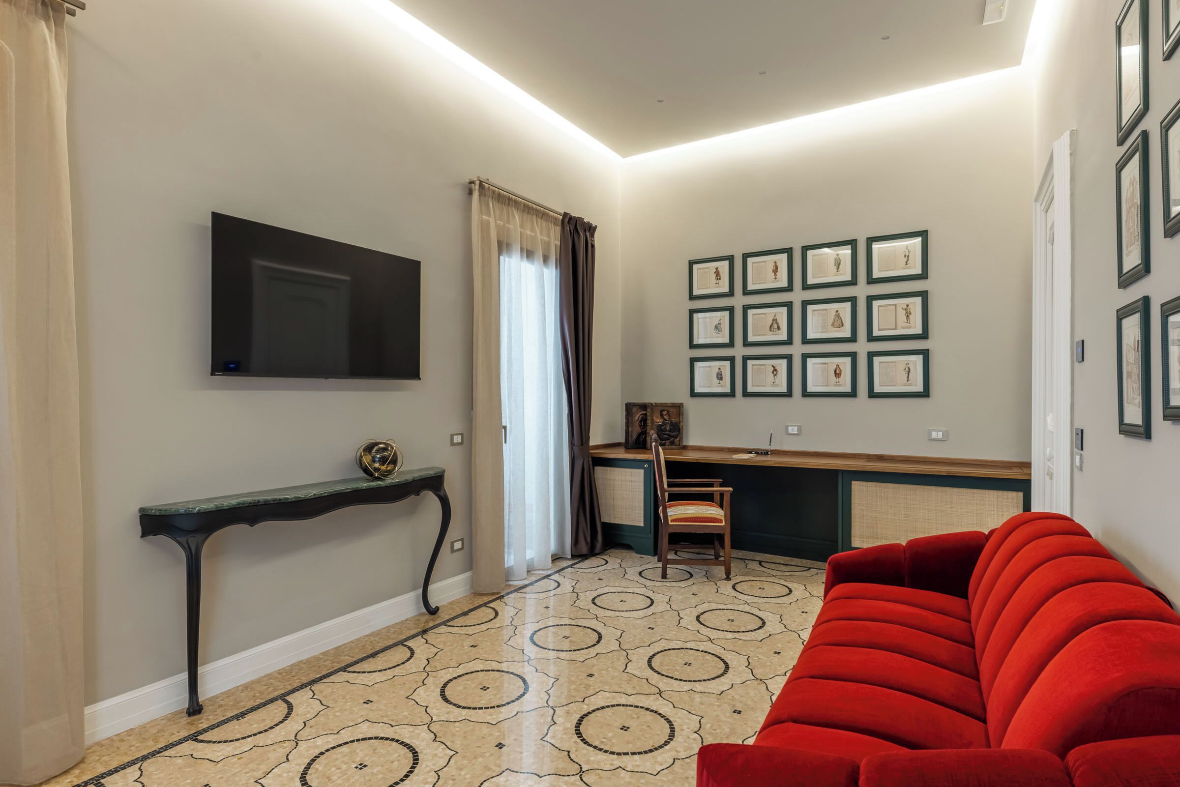 A living room with a red sofa, a TV mounted on the wall, a console table, and framed artwork on the wall.