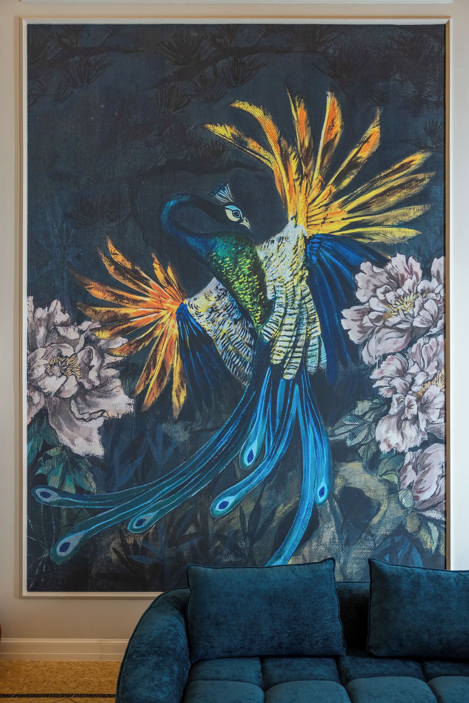 A large, colorful peacock painting on a wall, a plush blue sofa, and a patterned carpet.