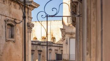 A narrow street with historic buildings, a metal railing, and people walking.