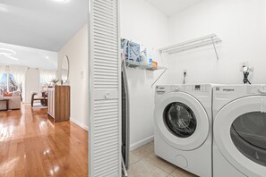 Ein Waschraum mit zwei weißen Whirlpool-Waschmaschinen, einem Wäscheständer und einem Regal mit Reinigungsmitteln.