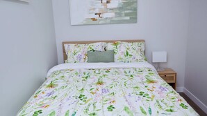 A bedroom with a floral bedspread, a wooden headboard, a bedside lamp, and a wall-mounted abstract painting. - Modern Basement Suite w/ Private Entrance (Winnipeg)