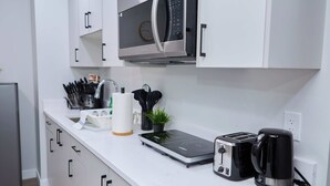 A modern kitchen with a microwave, toaster, kettle, and a small plant on the counter. - Modern Basement Suite w/ Private Entrance (Winnipeg)