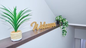 A wooden 'Welcome' sign, a potted plant, and a shelf with a plant. - Modern Basement Suite w/ Private Entrance (Winnipeg)