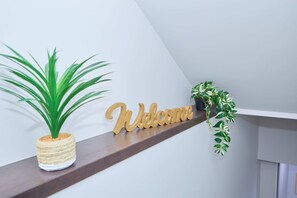 A wooden 'Welcome' sign, a potted plant, and a shelf with a plant. - Modern Basement Suite w/ Private Entrance (Winnipeg)