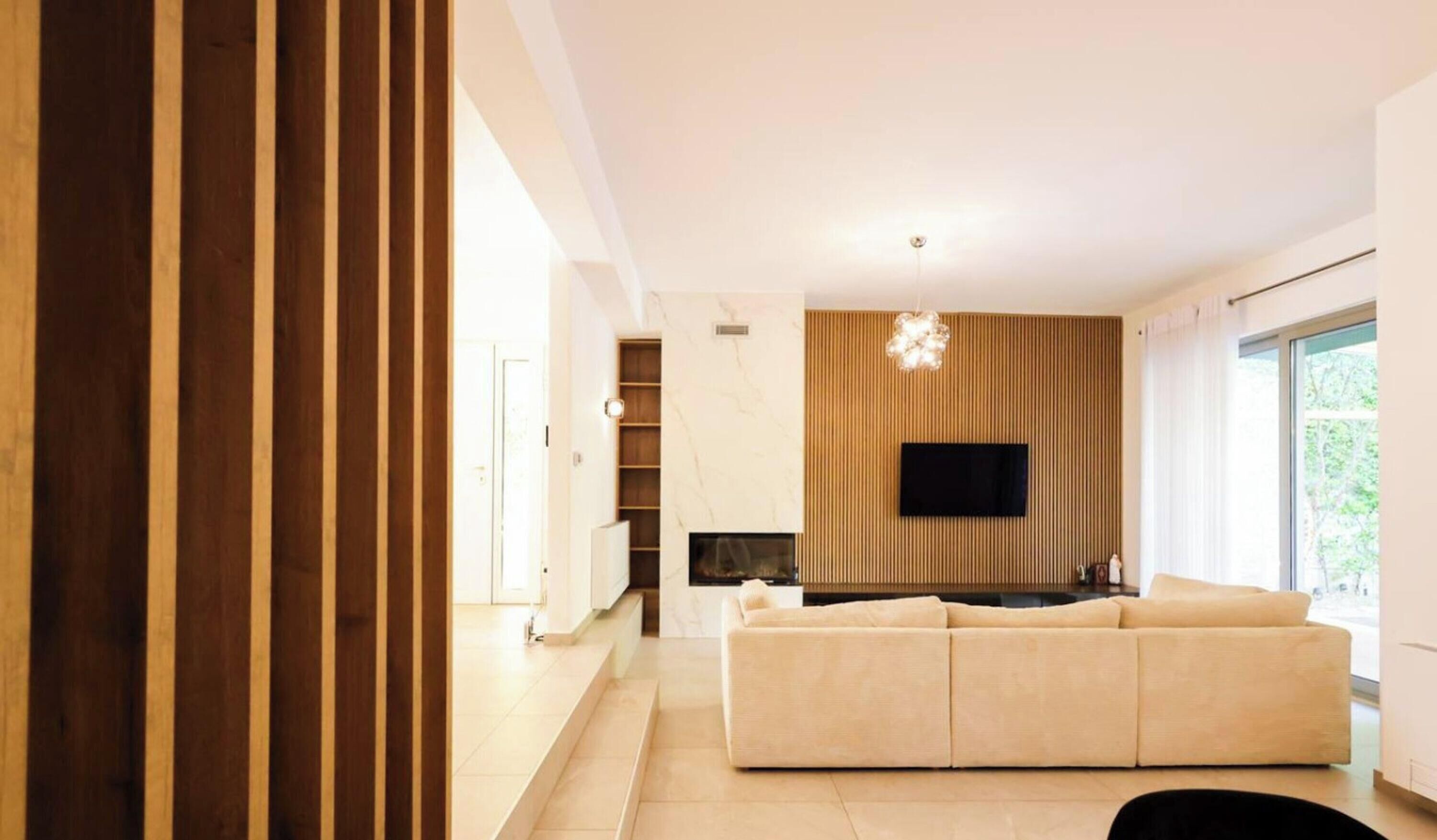 A modern living room with a sofa, a fireplace, a television mounted on the wall, and a large window.