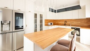 Una cocina moderna con armarios blancos, una isla de madera, electrodomésticos de acero inoxidable e iluminación colgante.