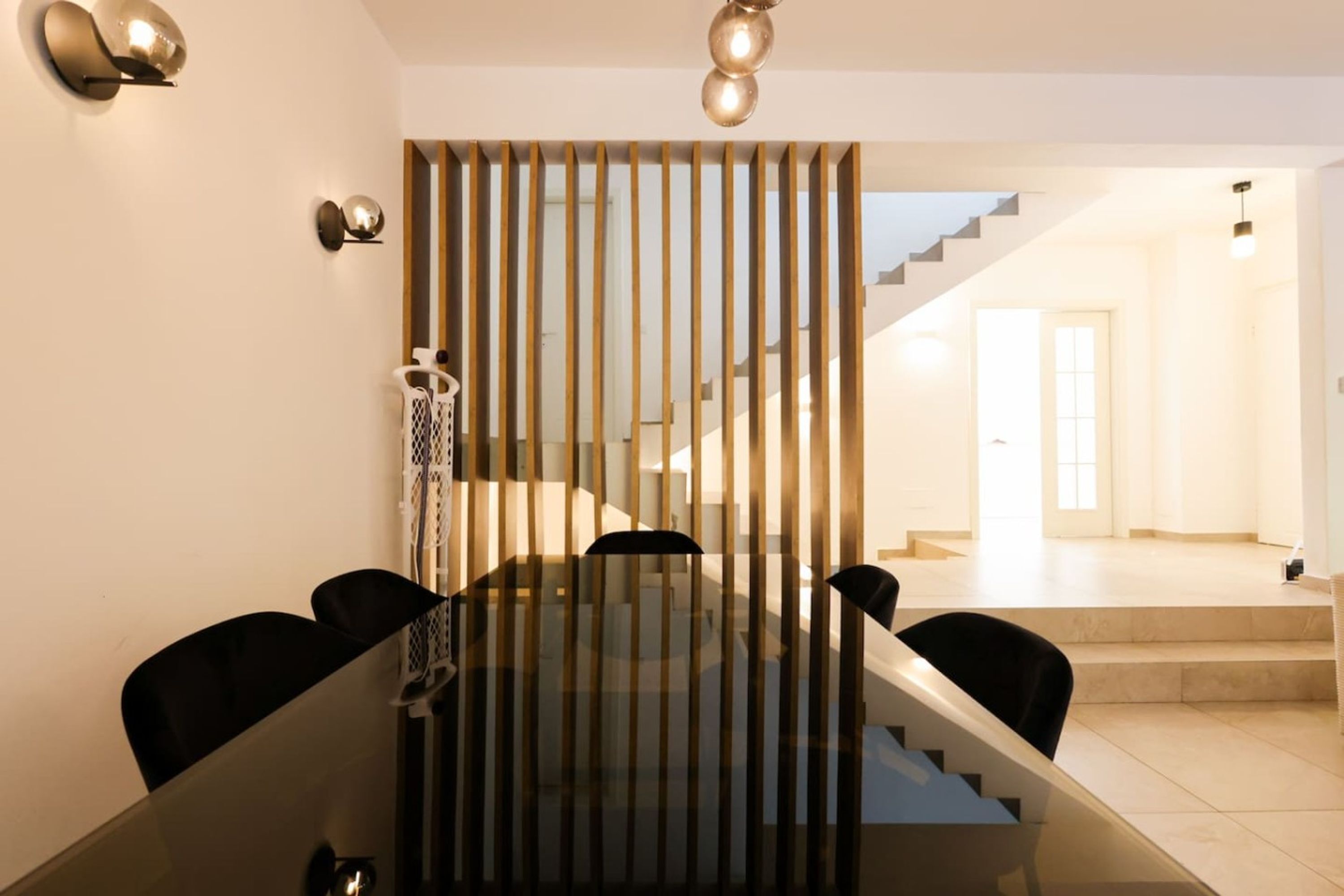A modern dining area with a glass table, black chairs, and a wooden partition with vertical slats.