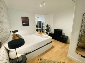 Ein modernes Hotelzimmer mit einem großen Bett, einem Flachbildfernseher, einem kleinen Schreibtisch und einer Topfpflanze.