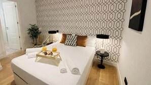 A hotel room with a bed, a tray with snacks, towels, a potted plant, and a wall with a geometric pattern. - C Madrid R o Est Ndar 2 Personas (Madrid)