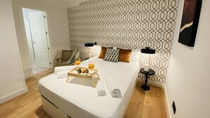 A modern hotel room with a large bed, geometric patterned wallpaper, a bedside table with a lamp, and a tray with breakfast items. - C Madrid R o Est Ndar 2 Personas (Madrid)
