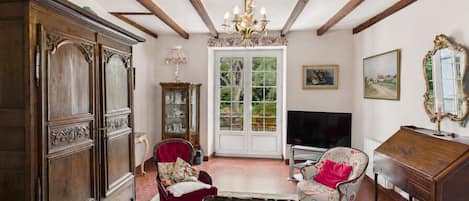 Una sala de estar con un mueble de madera, dos sillones, una mesa de centro, un televisor, un espejo y una puerta que da a un jardín.