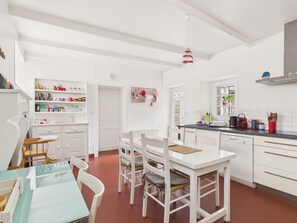 Une cuisine avec des meubles blancs, une table à manger avec des chaises et un luminaire suspendu.