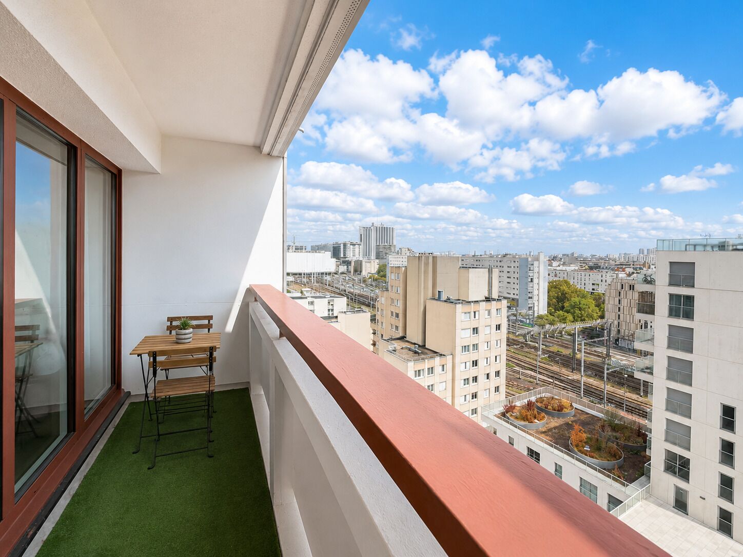 A balcony with a table and chairs, a view of the cityscape, and a green artificial turf floor.