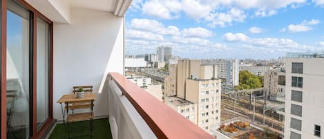 A balcony with a table and chairs, a view of the cityscape, and a green artificial turf floor.