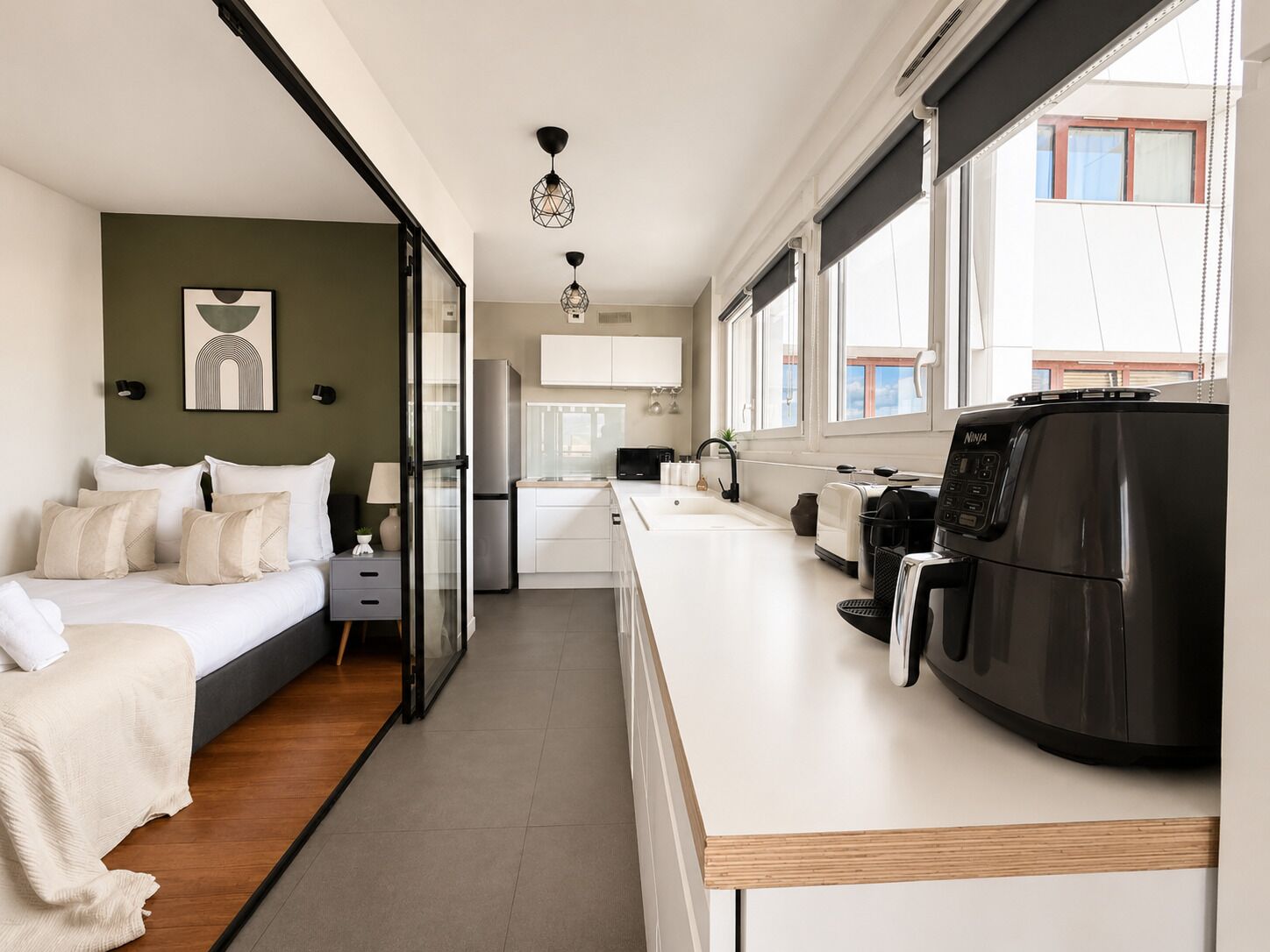 Une chambre d’hôtel moderne équipée d’un lit, d’une kitchenette et d’une grande fenêtre.