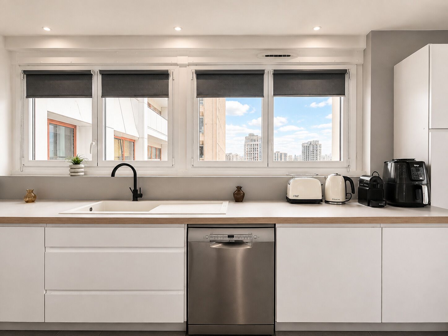 A modern kitchen with a built-in dishwasher, a double sink, and a window with blinds.