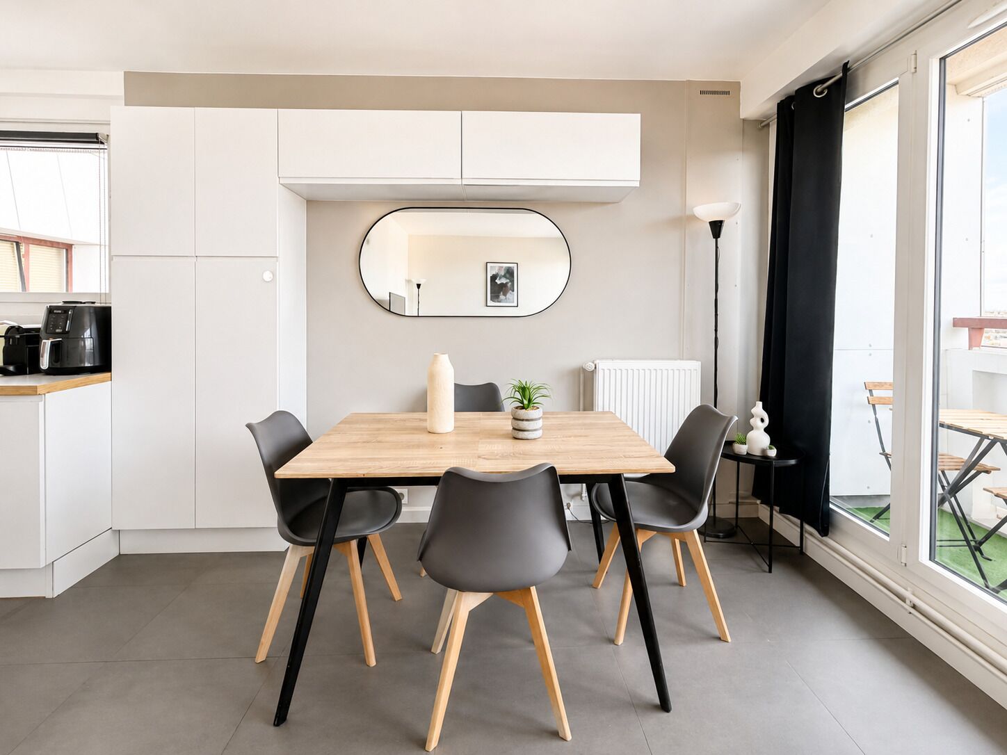 A modern dining area with a wooden table, black chairs, a white radiator, and a large window with a view.