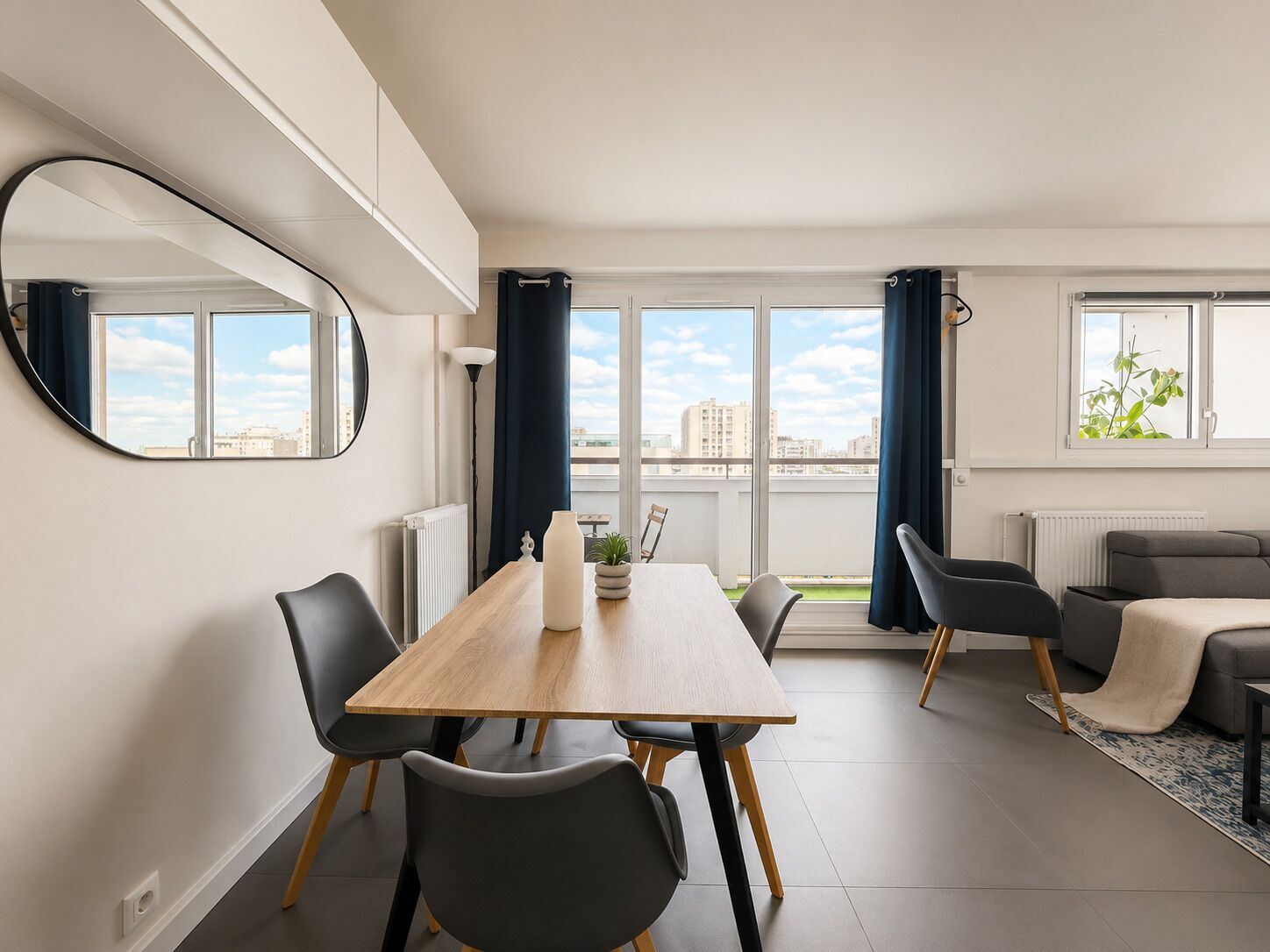 A modern living room with a dining area, large windows, and a view of the city.