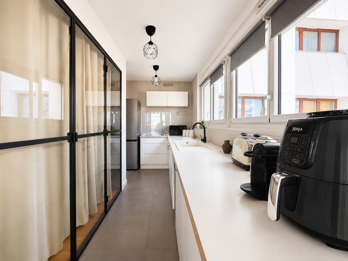 A modern kitchen with a built-in oven, a coffee machine, and a window with a view of the outside.