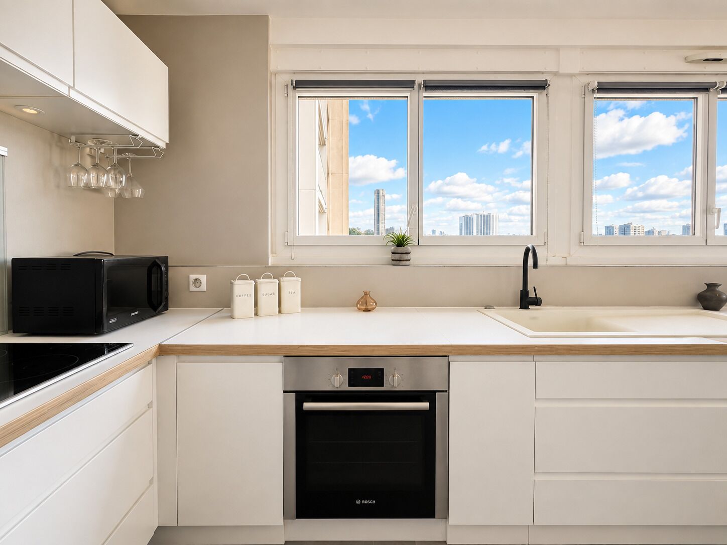 A modern kitchen with white cabinetry, a black microwave, a Bosch dishwasher, and a window with a city view.