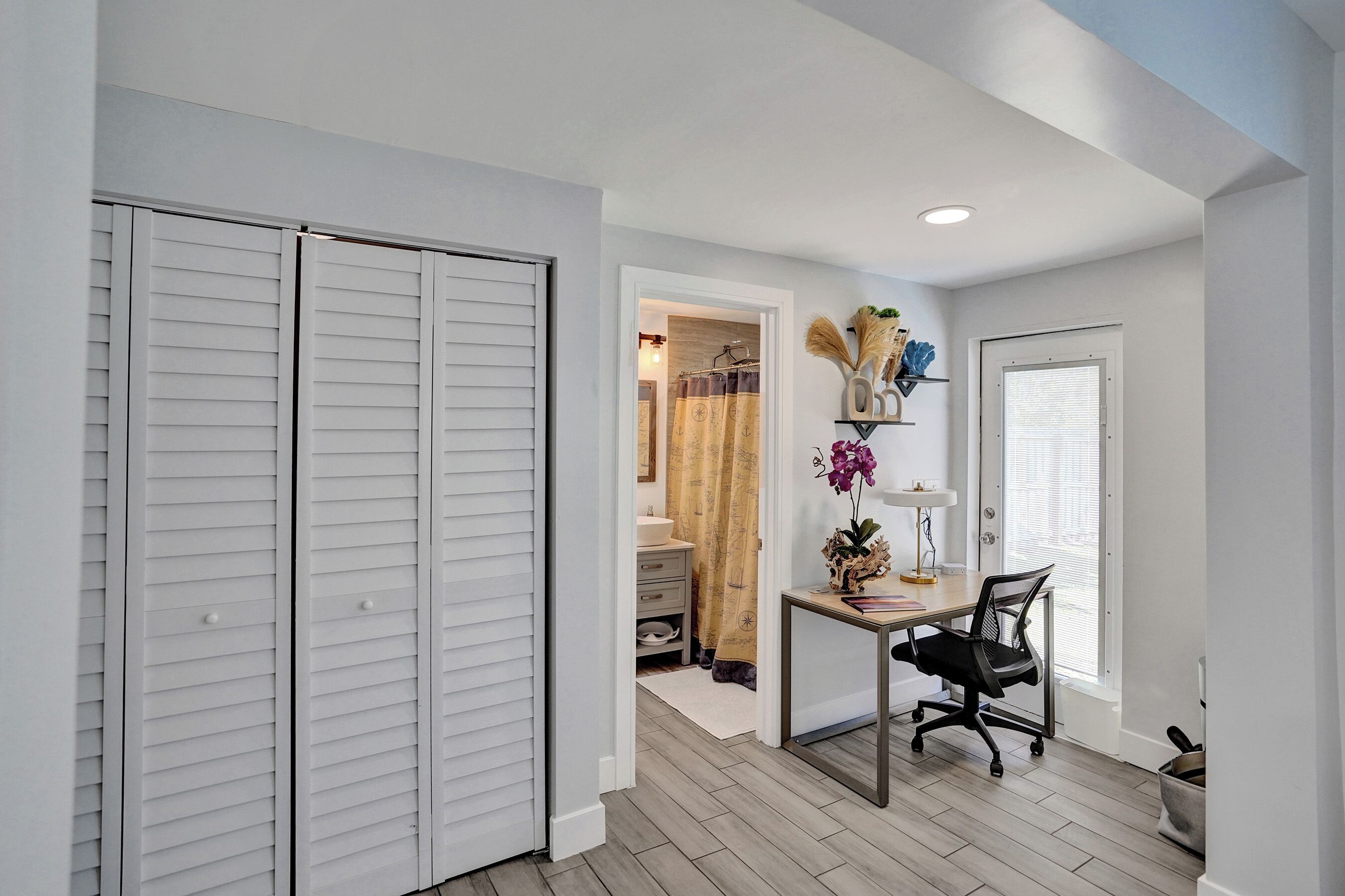 A room with a desk, chair, white closet, and a door leading to another room.