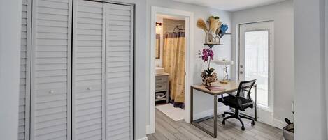 A room with a desk, chair, white closet, and a door leading to another room.