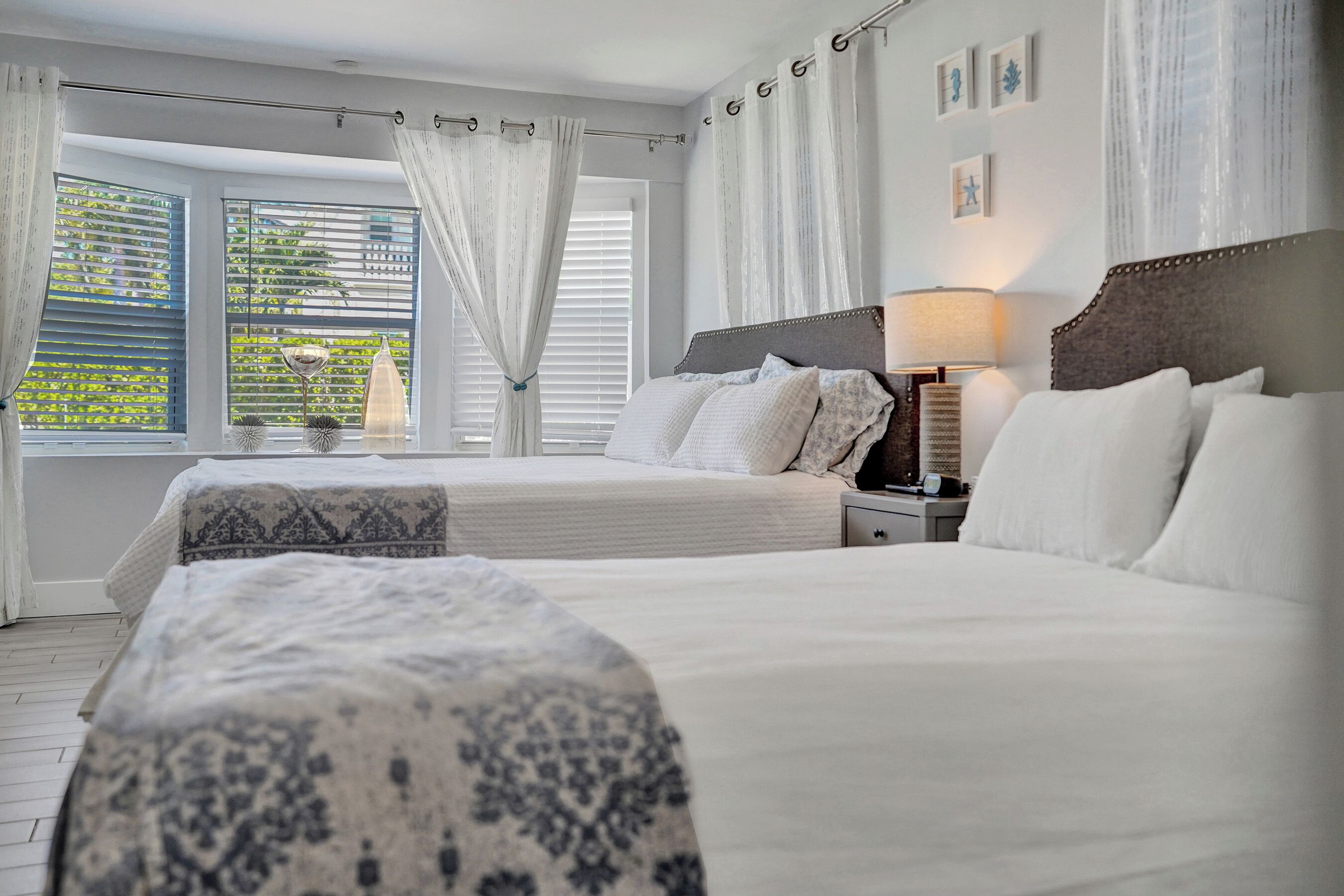 Une chambre d’hôtel avec deux lits, une table de chevet, une lampe et une fenêtre avec des rideaux.