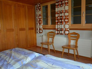 A bedroom with a bed, two wooden chairs, a window with curtains, and wooden wardrobes. - Rehweid (EG) Appartement/Fewo, Dusche oder Bad, WC 5-Bettwohnung by Interhome (Gstaad)