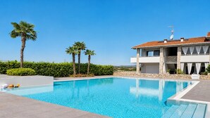 A swimming pool with a clear blue sky, a modern two-story building with stone facade, and palm trees. - Nala by Case al Lago (Castel Venzago)