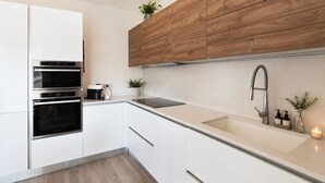 A modern kitchen with white cabinetry, a wooden accent wall, a stainless steel sink, and a built-in oven. - Nala by Case al Lago (Castel Venzago)