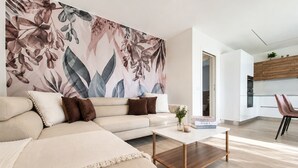 A modern living room with a sectional sofa, a coffee table, and a large floral wall mural. - Nala by Case al Lago (Castel Venzago)