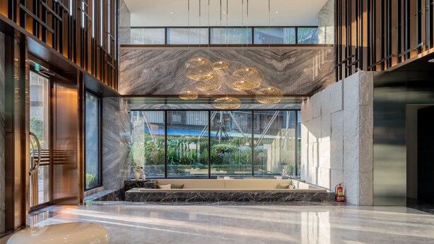 Um lobby moderno com piso de mármore, uma ampla janela com vista para o verde e um banco esférico exclusivo.