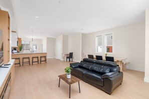 A modern living room with a leather sofa, a coffee table, and a dining area with a table and chairs. - Newly Built 3BR Townhome | Rooftop Patio & Garage (Langley)