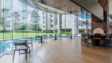 A modern indoor pool area with glass walls, wooden flooring, and multiple seating arrangements.