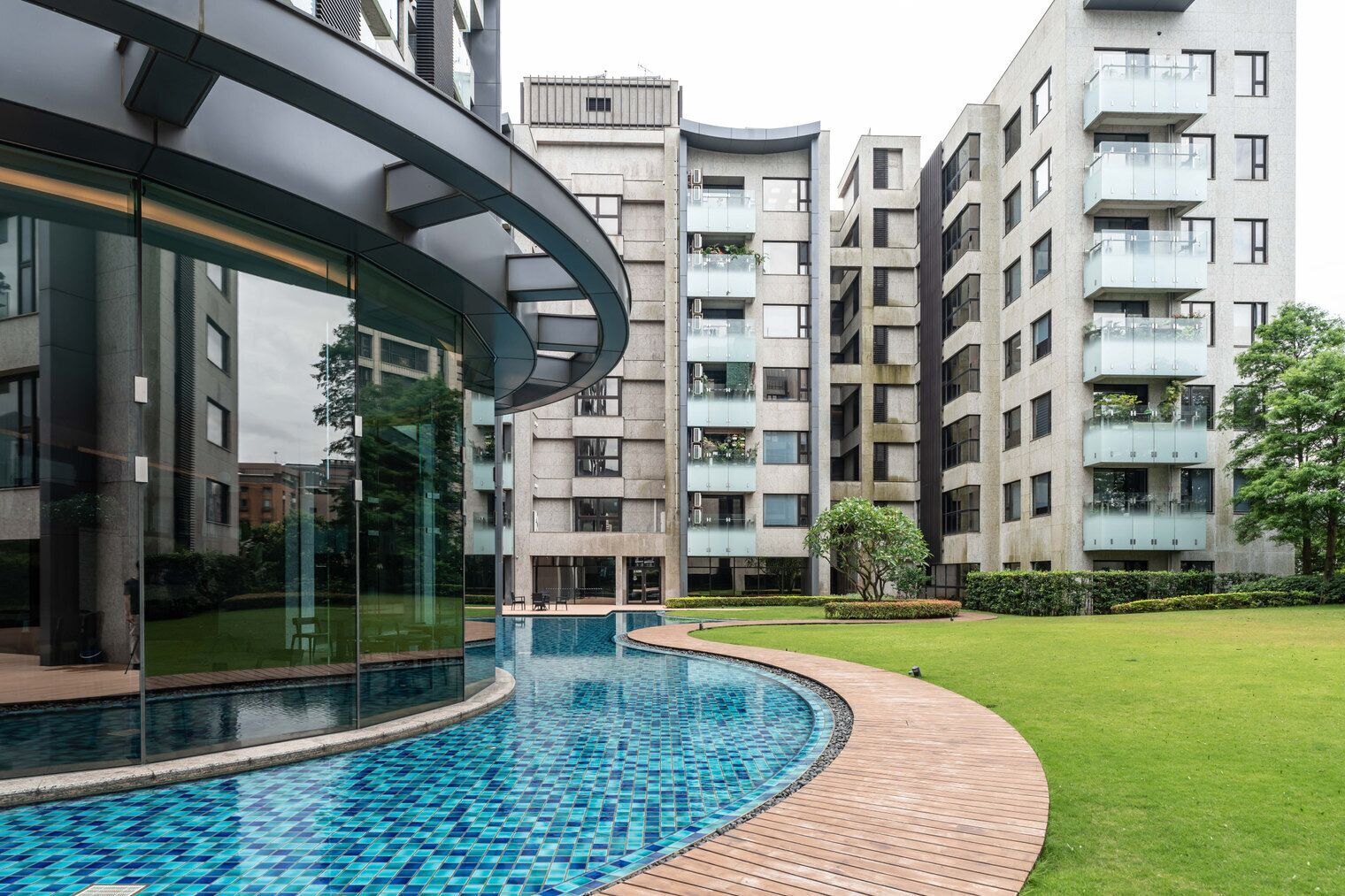 A modern building with a curved glass facade, a swimming pool, and a well-maintained lawn.