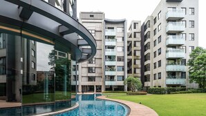 En moderne bygning med en buet glasfacade, en swimmingpool og en velplejet græsplæne.