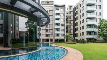 A modern building with a curved glass facade, a swimming pool, and a well-maintained lawn.