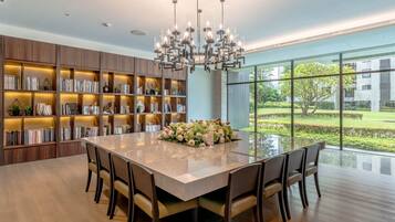 A modern kitchen with a large island, built-in bookshelves, and a view of a garden through large windows.