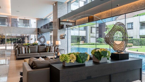 En moderne lobby med en sofa, et konsolbord med blomster og udsigt til en pool og grønne områder.