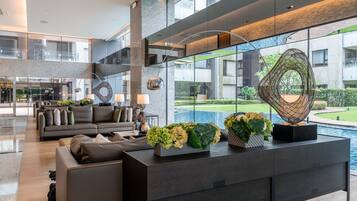 A modern lobby with a sofa, a console table with flowers, and a view of a pool and greenery.