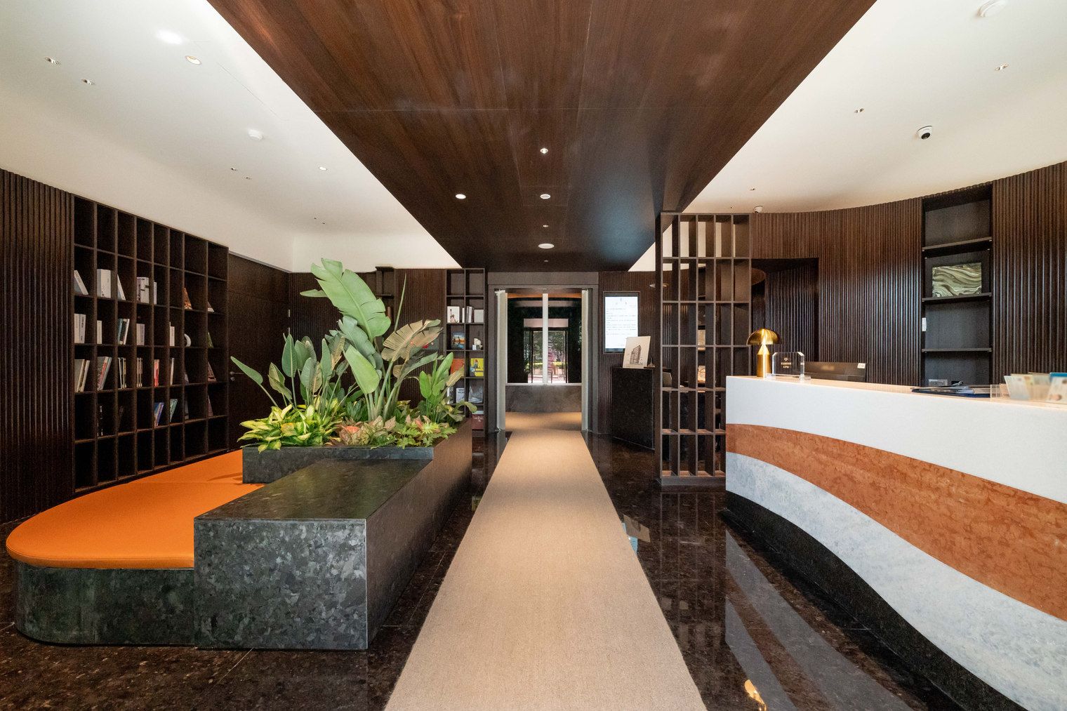 A modern reception area with a reception desk, a seating area with a planter, and bookshelves.