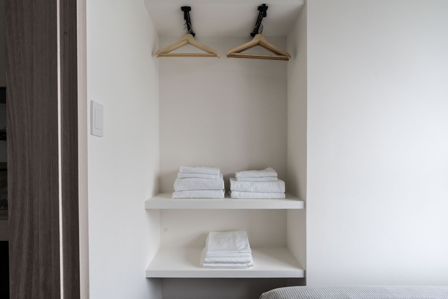 A white wall with two wooden hangers and three white shelves.