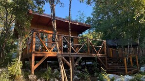 A wooden cabin with a deck, surrounded by trees and rocks. - Bungalow with Patio (Rvaši)