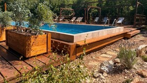 A swimming pool with wooden deck and lounge chairs, surrounded by greenery. - Bungalow with Patio (Rvaši)