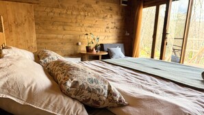 A wooden cabin bedroom with a bed, pillows, a small table, and a window. - Bungalow with Patio (Rvaši)