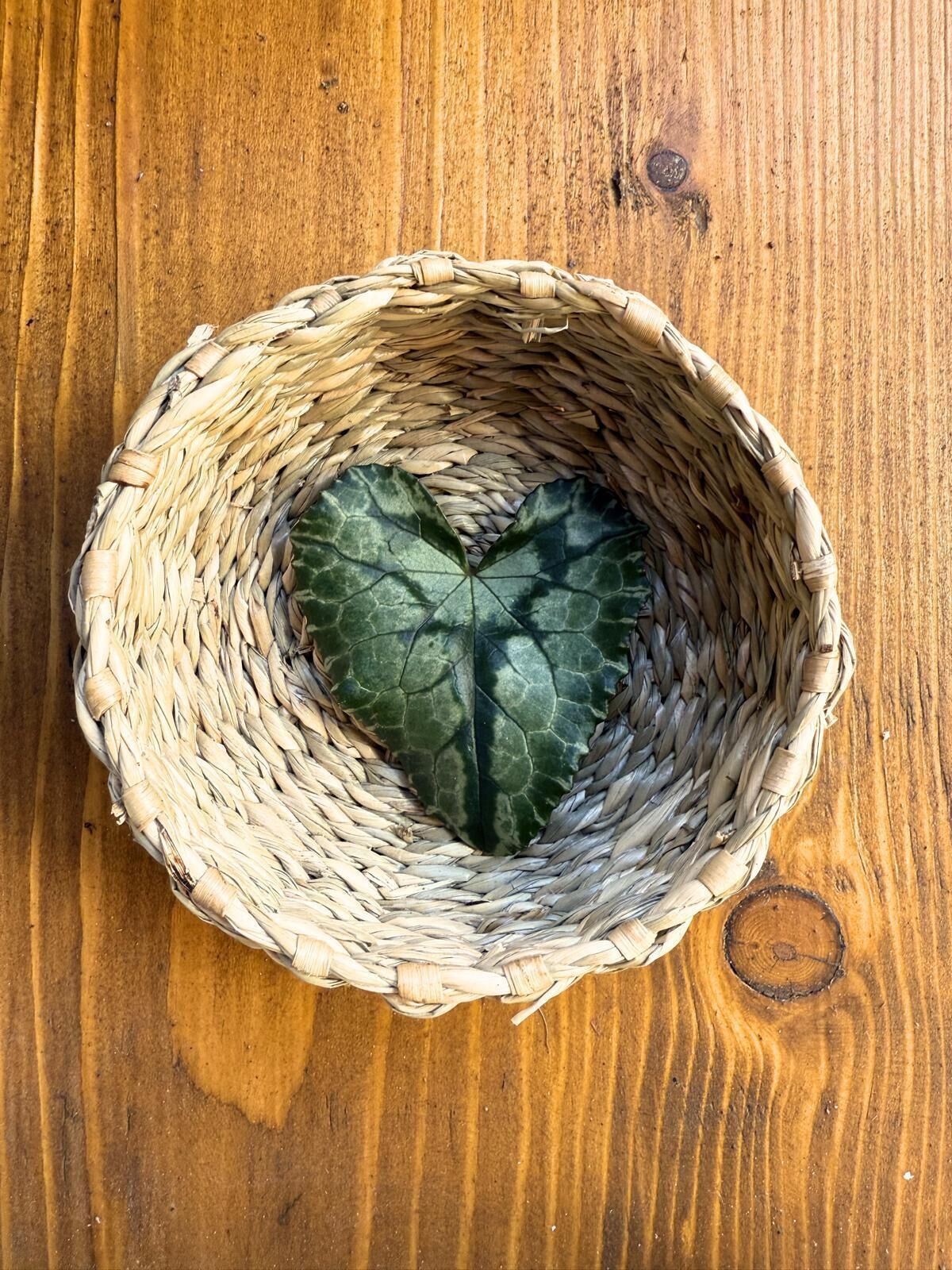 Una cesta tejida con una hoja con forma de corazón sobre una superficie de madera.
