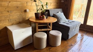 A cozy room with a wooden wall, a gray sofa, a small round table with plants, a white cabinet, and two ottomans. - Bungalow with Patio (Rvaši)