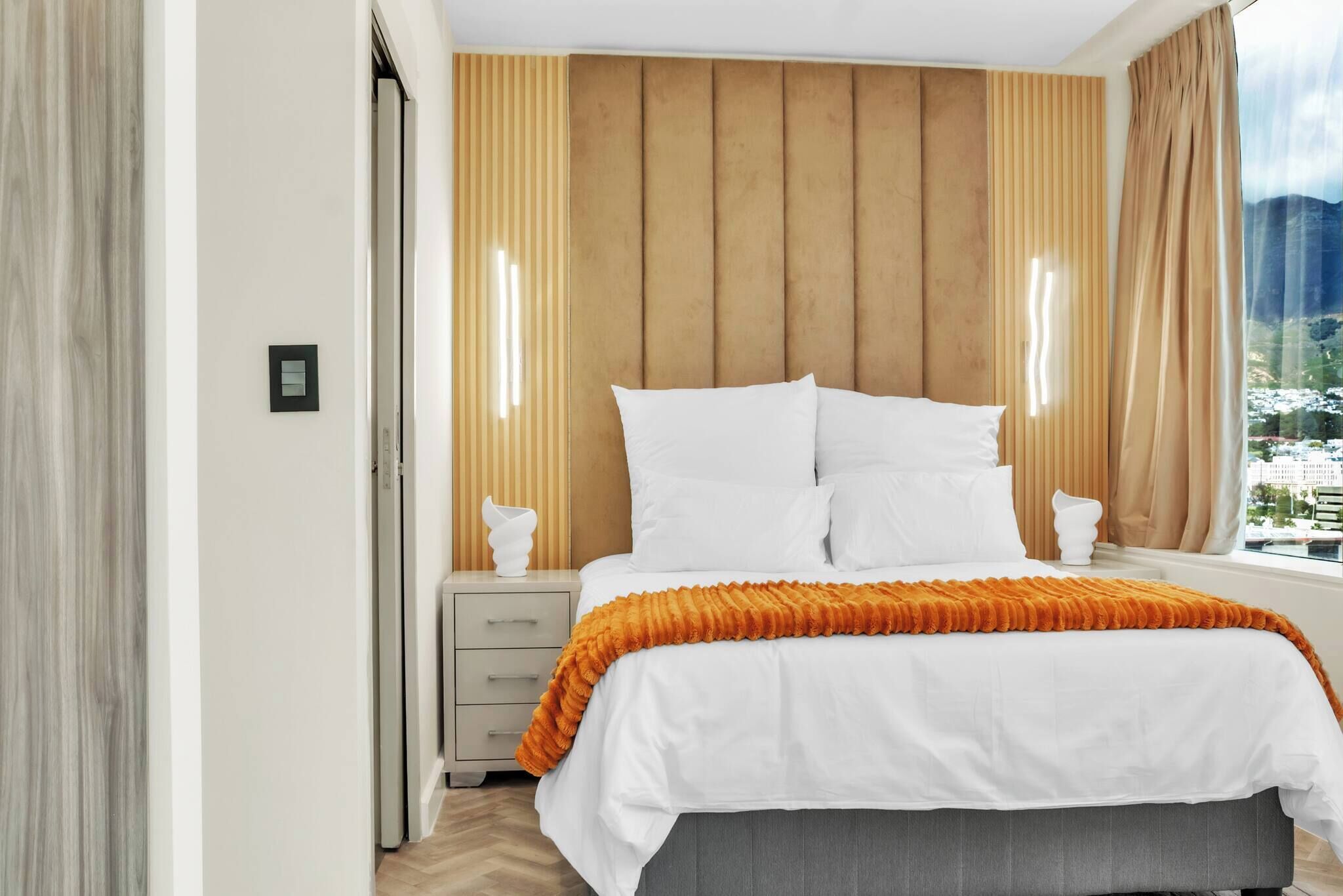 Un dormitorio con cama, mesitas de noche, una ventana con cortinas y un cabecero de madera.