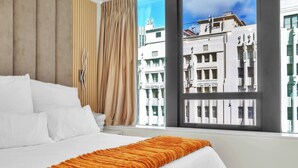 A hotel room with a bed, a window with a city view, a curtain, and a wooden panel wall. - Softstay, Foreshore Cape Town CBD (Cape Town)
