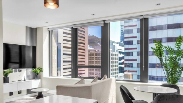 A modern hotel room with a large window, a flat-screen TV, a sofa, a dining table, and a potted plant. - Softstay, Foreshore Cape Town CBD (Cape Town)